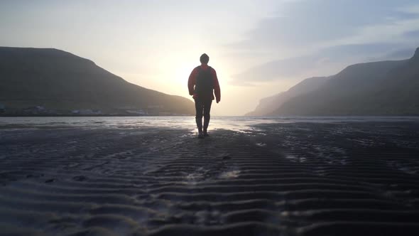 Man Walking Along Lake At Low Tide At Sunrise alt
