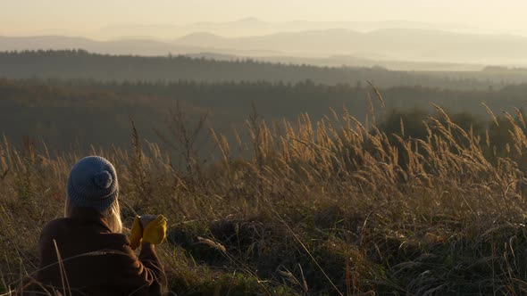 Beautiful girl with mug of tea in mountains Sudetes in November in sunset alt