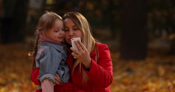 Cute Little Girl in Black Jacket Looks at the Yellow Leaves and Rejoices in the Autumn Park with Her