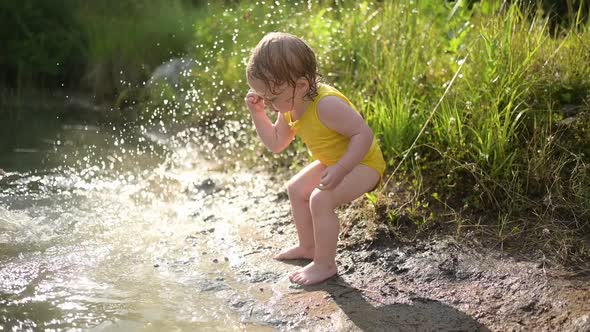 Little Funny Cute Blonde Girl Child Toddler in Yellow Wet Bodysuit Playing By the Lake Waterside