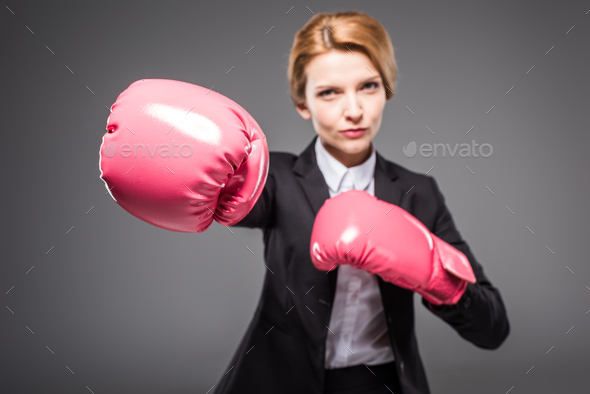 selective focus of businesswoman in suit and pink boxing gloves, isolated on grey
