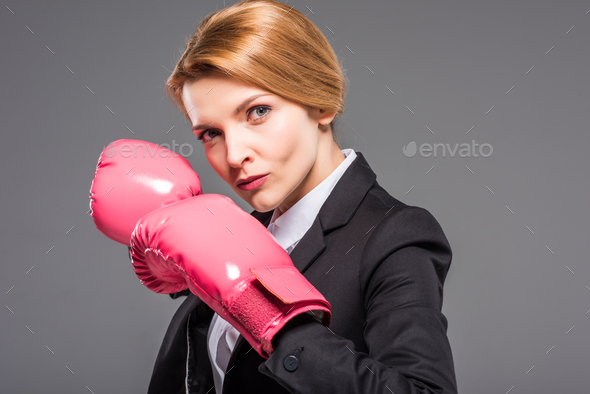 portrait of serious businesswoman posing in pink boxing gloves, isolated on grey