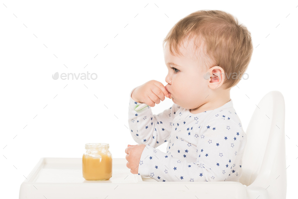 Baby boy in high chair eating pureed food with spoon - Stock Image