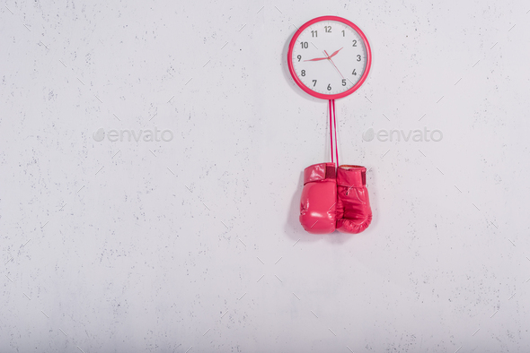 pink boxing gloves hanging at wall clock on white
