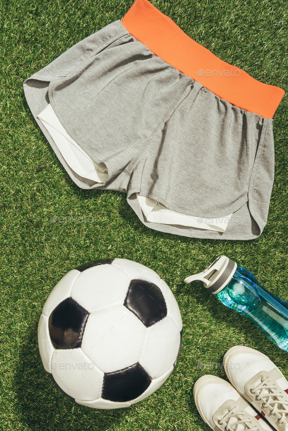 flat lay with soccer ball, sportswear, water bottle and sneakers on green grass