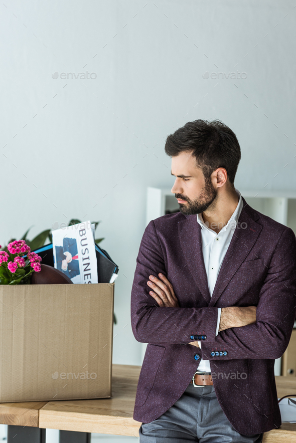 thoughtful young businessman looking at box of personal stuff in office after he gets fired