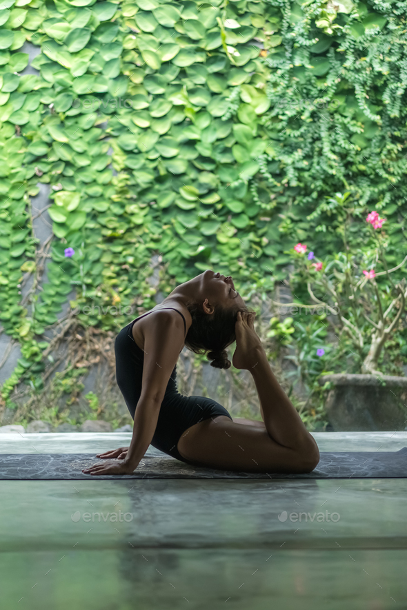 Side view of beautiful young woman practicing yoga and performing back bend with feet touching head