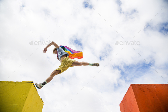 young man jumping through the air with gay pride flag cape on his back - Stock Photo - Images