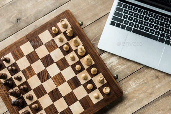 Laptop and chess board with figures on rustic wooden surface