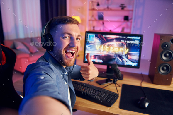 Making selfie. Screaming and celebrating victory. Online streamer playing FPS shooter game at home