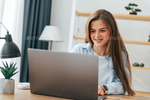 Working by using laptop. Young beautiful woman is home alone in domestic room - Stock Photo - Images
