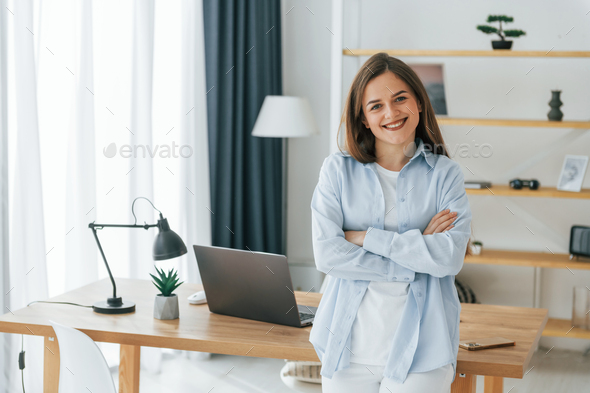 Standing with arms crossed. Young beautiful woman is home alone in domestic room - Stock Photo - Images