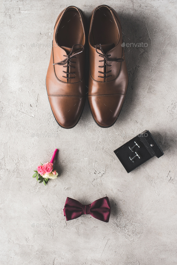 top view of brown shoes, cufflinks, bow tie and boutonniere on gray surface - Stock Photo - Images