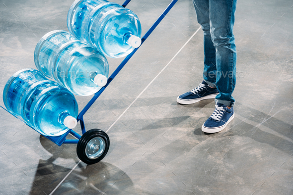 Close-up view of loader man standing by cart with water bottles