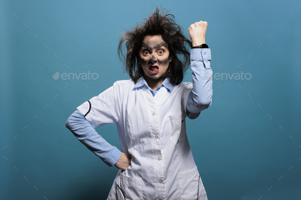 Crazy scientist with dirty face and wacky hair angrily clenching and raising fist in air while
