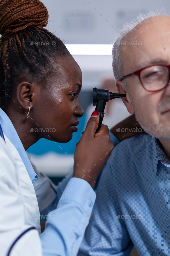 Close up of hospital specialist examining retired man using otoscope
