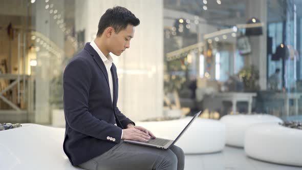 Young Asian Male Businessman in Suit Working with Laptop on His Knees