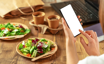 Female holding smartphone and and makes an order of healthy food through mobile app.