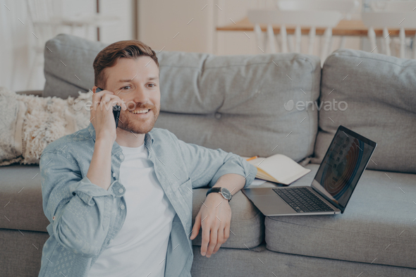 Young male company employee working remotely from home calling boss to tell good news