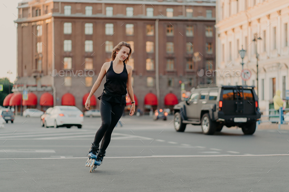 Active girl rollerblading on grey asphalt poses on rollers dressed in active wear drives fast