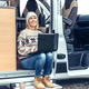 Woman teleworking sitting in the door of a camper van - PhotoDune Item for Sale