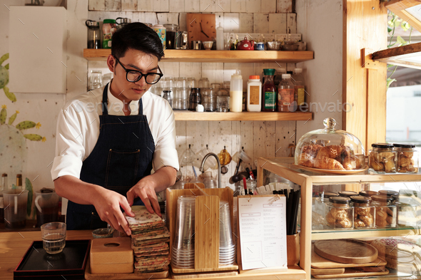 Young Vietnamese barista arranging coffee cup sleeves on counter