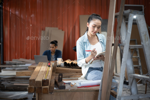 Young Asian designer furniture woman Carpenter uses a tape measure to measure chair on the workbench