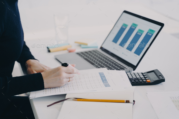 Hands of european woman at the desk in office. Entrepreneur is working at laptop and calculating. - Stock Photo - Images