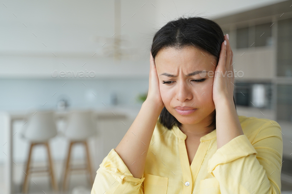 Irritated angry female renter cover ears with hands suffer from loud music, noisy neighbors at home