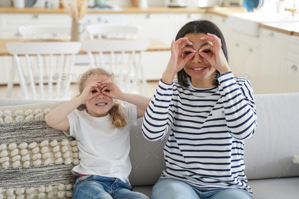 Mother, daughter fool around do funny faces make binoculars with fingers having fun together at home