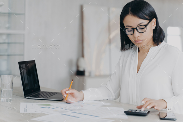 Remote accountant is calculating profit. Young hispanic bookkeeper is working distantly from home. - Stock Photo - Images
