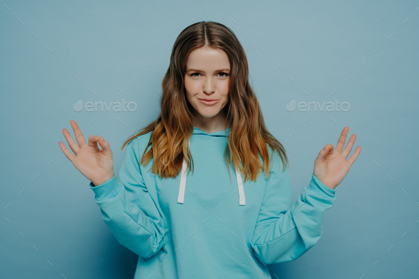 Smiling teenager girl showing okay sign standing against blue wall - Stock Photo - Images