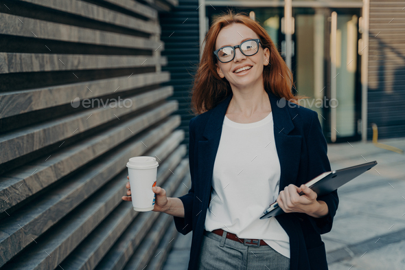 Redhead woman enjoys walk outdoor drinks takeaway coffee carries digital electronic device notepad - Stock Photo - Images