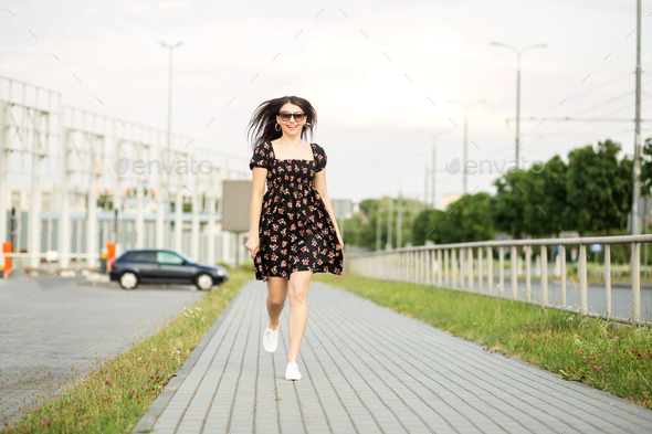 An adult smiling woman walks down the street in a stylish dress. The concept of the style of life