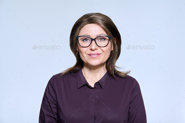 Mature smiling woman in glasses looking at camera on light background ...