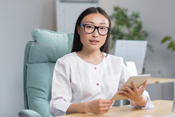 Online admission to the hospital. A young beautiful Asian woman doctor with tablet - Stock Photo - Images