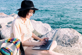 young woman with computer and backpack by the sea