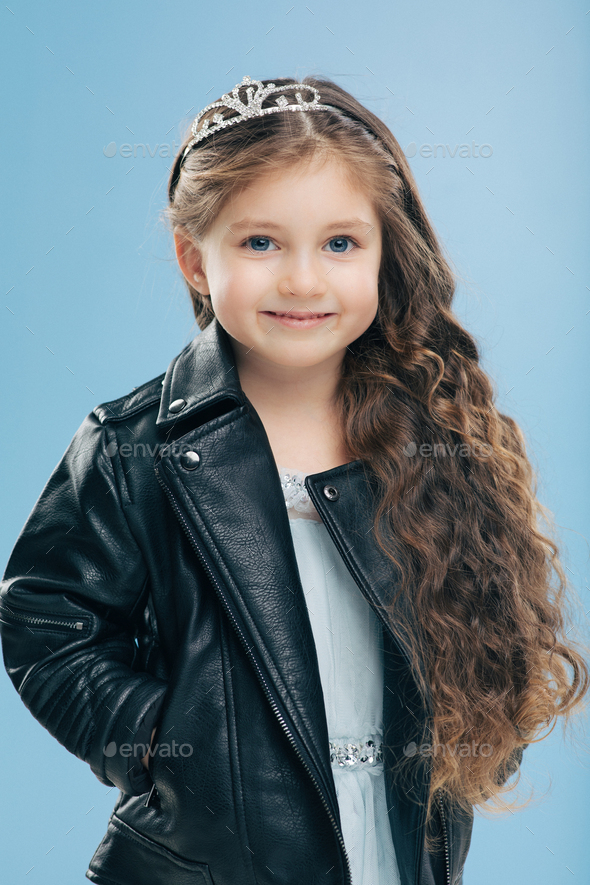 attractive small female child has long curly hair, wears crown and ...