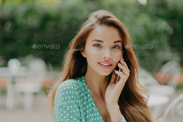 Horizontal shot of pretty young woman wears polkadot blouse, makes phone call