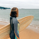 Surfer woman with wetsuit carrying surfboard looking to the sea at the beach - PhotoDune Item for Sale