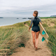 Surfer woman with wetsuit and surfboard going to the beach through the dunes - PhotoDune Item for Sale