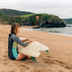 Surfer woman with wetsuit and surfboard sitting on the sand looking at the sea - PhotoDune Item for Sale