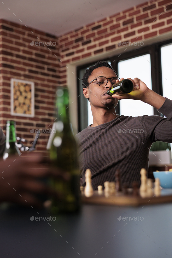 Pensive african american man thinking about next chess move while sitting  at table. Stock Photo by DC_Studio