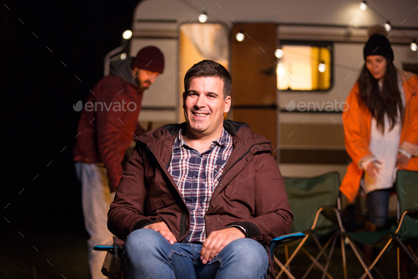 Tourist in a camp site smiling while his friends are making camp fire