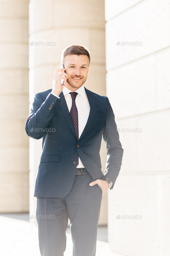 Vertical shot of handsome successful male financial director solves problems via smart phone