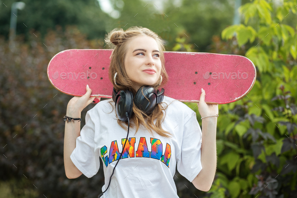 Teen girl with skateboard. Listen to music on headphones. Concept of an active lifestyle, hobby
