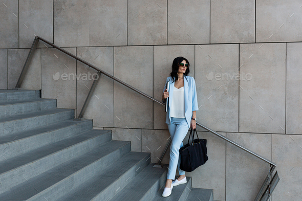 Beautiful young business woman with a laptop in her hands walks up the stairs to the office
