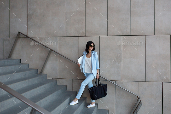 Beautiful young business woman with a laptop in her hands walks up the stairs to the office