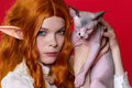 Portrait of young female cosplayer elf showing purebred Sphinx kitten with blue eyes - PhotoDune Item for Sale