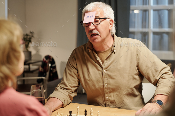 Senior man with notepaper on his forehead asking questions to aged woman